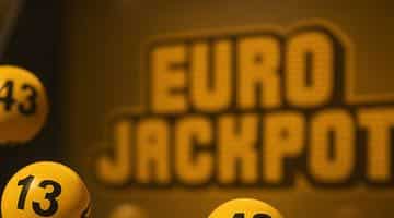 Gula numrerade bollar snurrar i en lotterimaskin under en Eurojackpot-dragning. I bakgrunden syns loggan för Eurojackpot.