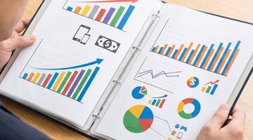 En person håller i en ekonomisk rapport med grafer och diagram. Bilden ska illustrera någon som läser en ekonomisk rapport om omsättningen på den svenska spelmarknaden.