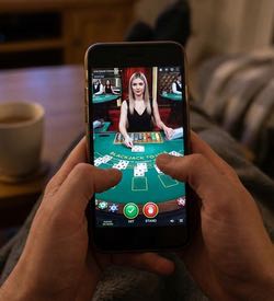En person sitter med benen på soffbordet och spelar live casino i mobilen.