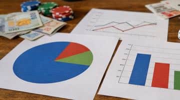 Papper med diagram och grafer med statistisk data på ett bord tillsammans med spelrelaterade objekt som pokerchips och kontanter